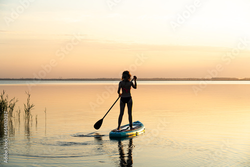 Sports girl on board for glanders surfing. young slender woman floats on a board with a paddle. Surfing. Summer fun on the water. Healthy lifestyle. Woman stand up paddle boarding SUP on calm water