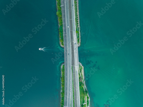Aerial view of vehicles driving on a road crossing the Lugano lake with a bridge and a boat sailing under the bridge, Melide, Ticino, Switzerland. photo