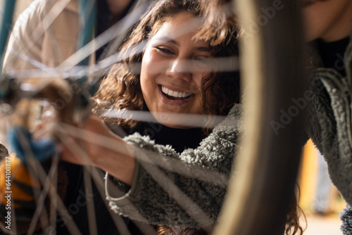 Happy female technician seen through bicycle wheel spokes at recycling center