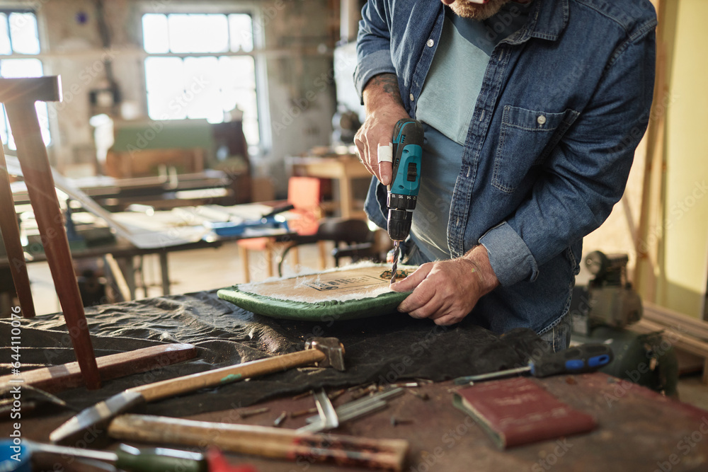 Closeup of senior man repairing old furniture in carpentry workshop and holding electric drilling tool, copy space Closeup of senior man repairing old furniture in carpentry workshop and holding electric drilling tool, copy space