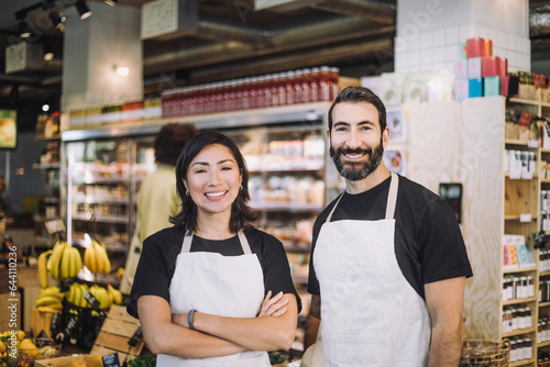 Portrait of smiling multiracial male and female retail clerks wearing aprons standing at grocery store photo