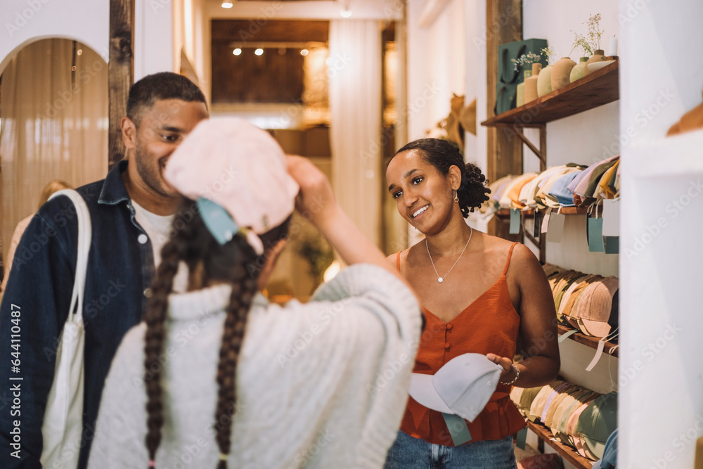 Smiling saleswoman and man looking at girl wearing cap in fashion clothing store Smiling saleswoman and man looking at girl wearing cap in fashion clothing store