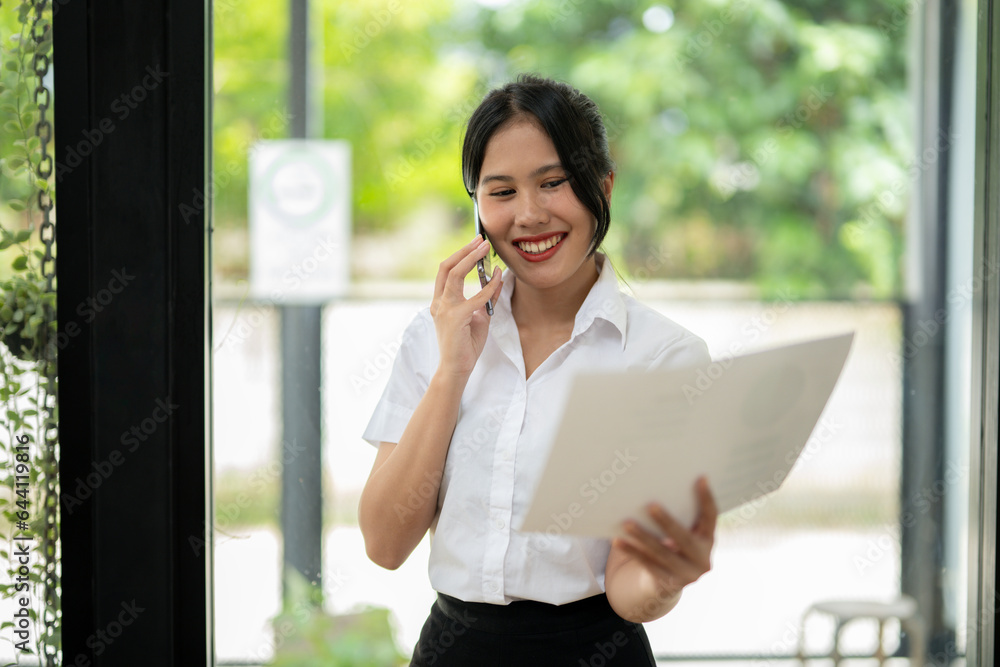 Businesswoman talking on the phone with friend or colleague while checking documents in modern office Businesswoman talking on the phone with friend or colleague while checking documents in modern office