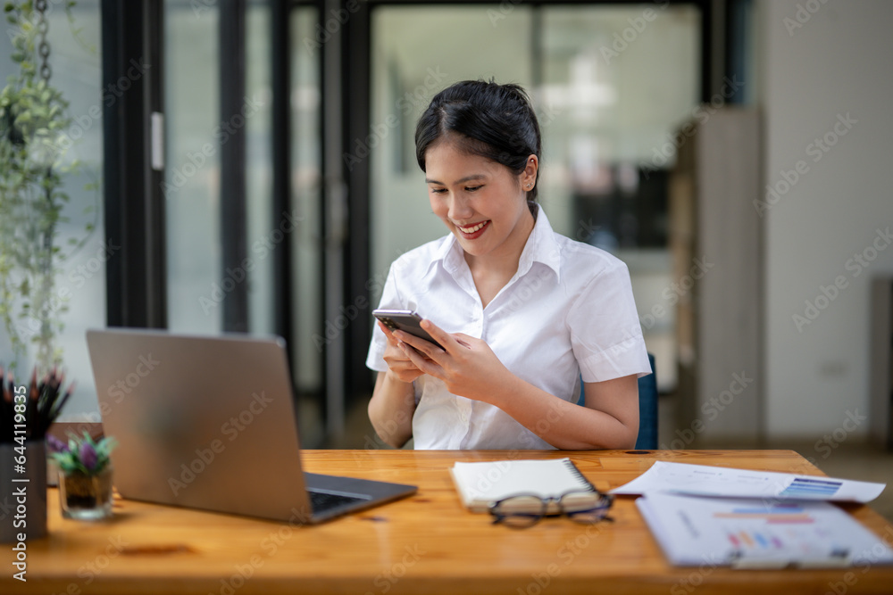 Businesswoman sitting in front of laptop and engrossed in typing chat on phone... Businesswoman sitting in front of laptop and engrossed in typing chat on phone...