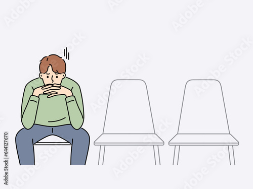 Sad man is waiting for start of interview, sitting in office corridor with empty chairs. Guy is nervous before interview because of problems in labor market and difficulty of finding well-paid job