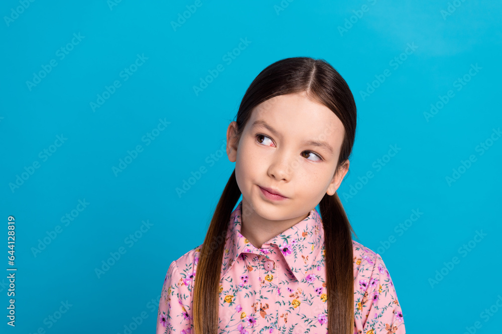 Photo portrait of lovely schoolkid girl look interested empty space wear trendy pink flower print garment isolated on blue color background Photo portrait of lovely schoolkid girl look interested empty space wear trendy pink flower print garment isolated on blue color background