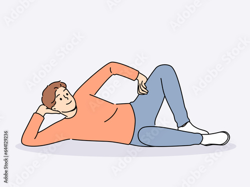 Man lies on floor with hand under head and with smile looks at screen, offering to relax and unwind. Happy guy lies on ground and smiles, feeling lazy orlacking initiative for personal growth.