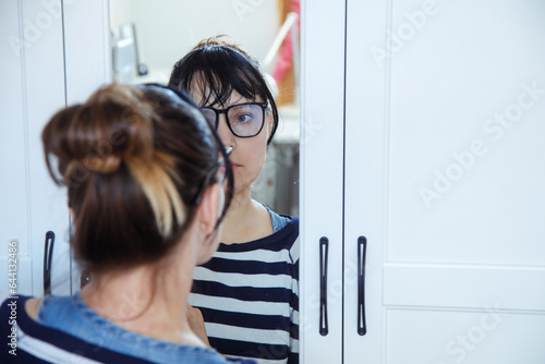 Reflection in mirror of deeply thoughtful young pretty woman in black-rimmed glasses. Emotions and experiences. 