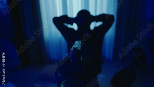 The arrest of a burglar in a dark apartment lit by blue light. The offender is on his knees, with his hands up. A gun in the hand of a policeman on a blurred background of a criminal close up.