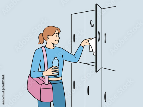 Woman visitor to gym stands near lockers for personal belongings and prepares for sports workout. Girl with bag for sportswear and bottle of water visits gym to maintain good figure