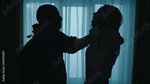 Defenceless and in danger. A robber in a black balaclava holds a frightened woman by the neck, strangling her close up.