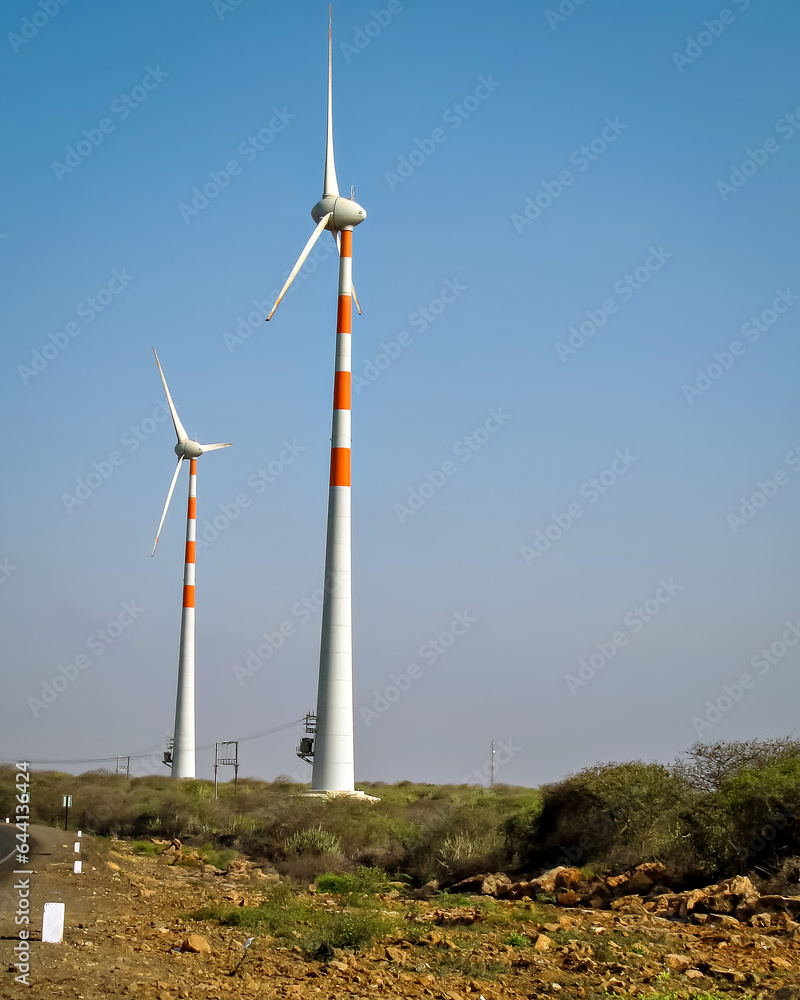 Tall Windmills distributed in an open field with nice, clear blue sky background