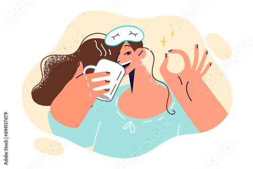 Cheerful woman in sleep mask drinks coffee and shows OK gesture, rejoicing at start new working day