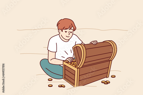 Treasure hunter boy found wooden chest with gold and is sitting on beach looking at prey. Little kid dreams of finding sunken treasure of pirates from middle ages and getting rich.