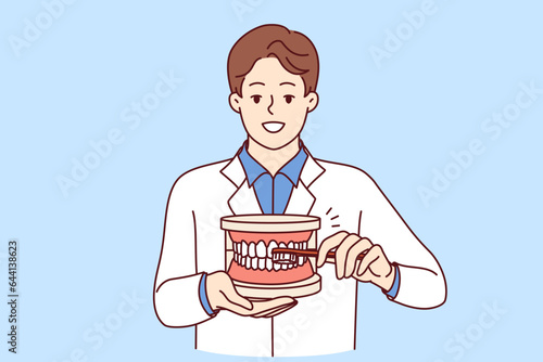 Man dentist explaining rules of brushing teeth, holding toothbrush and giant jaw in hands. Guy dentist recommends observing hygiene requirements to avoid appearance of caries in mouth