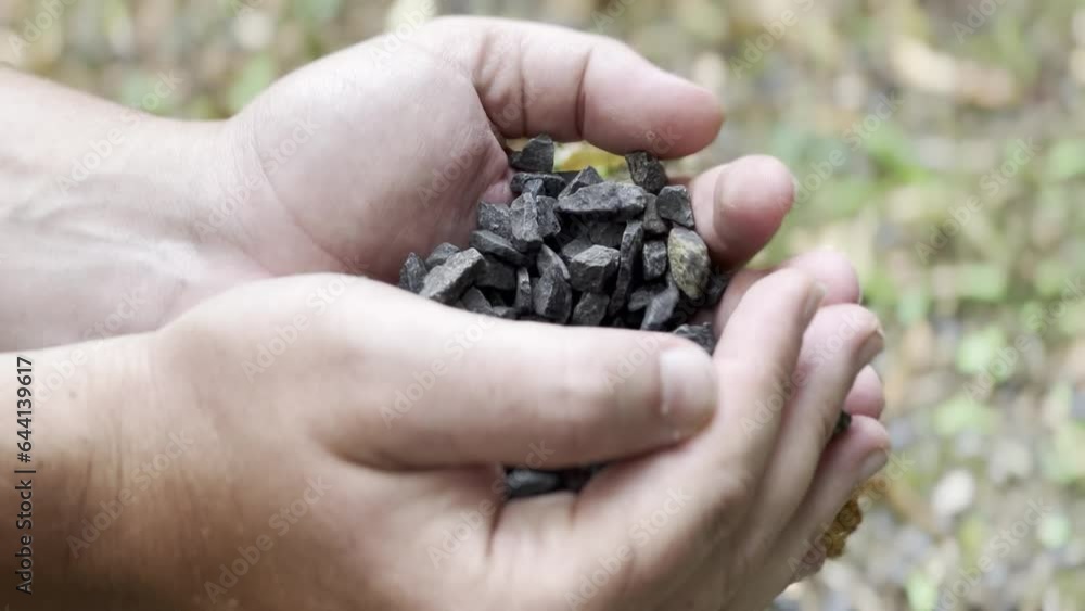 Little black rocks pouring out from a human hands and falling down Little black rocks pouring out from a human hands and falling down