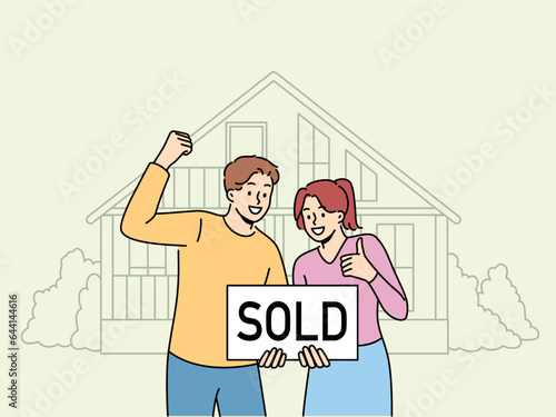 Happy couple is standing near house with inscription sold, rejoicing in sale of real estate at bargain price. Satisfied man and woman rejoice in profitable real estate deal and make victory gestures