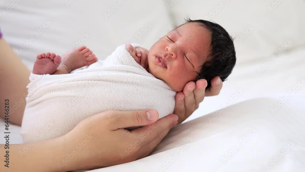mom's hands of a white-skinned woman are rocking a newborn African-American baby in a diaper, soothing him before going to bed, a small child is lying on the bed in the bedroom in close-up mom's hands of a white-skinned woman are rocking a newborn African-American baby in a diaper, soothing him before going to bed, a small child is lying on the bed in the bedroom in close-up