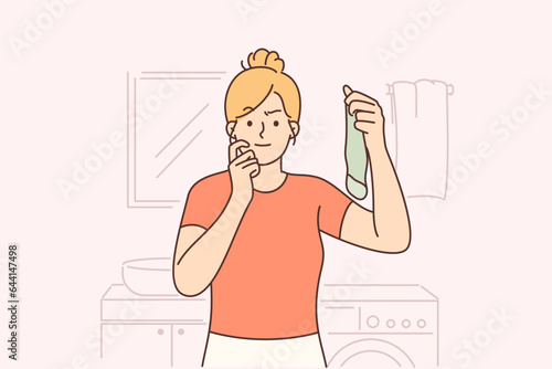 Housewife holds dirty sock standing in laundry room and looks at screen in embarrassment