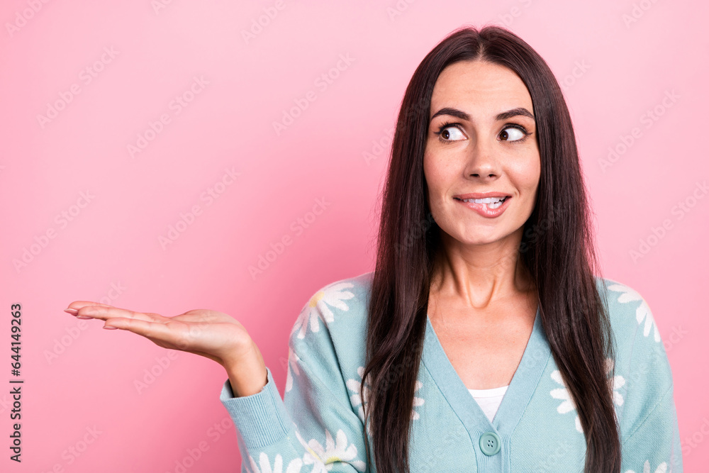 Portrait of astonished girl wear flower print pullover look at arm presenting empty space biting lip isolated on pink color background Portrait of astonished girl wear flower print pullover look at arm presenting empty space biting lip isolated on pink color background