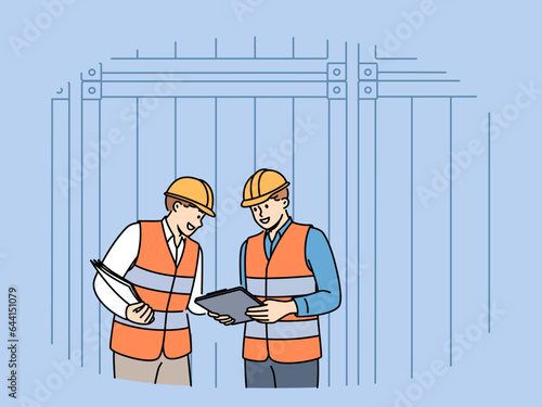 Men work in industrial field and stand near sea shipping containers discussing logistics or storage cargo. Teamwork of transport company employees dressed in industrial uniforms and hardhat