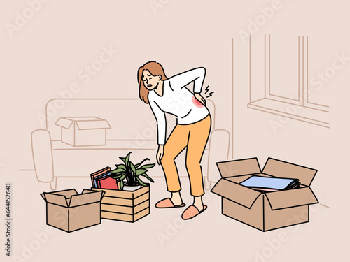 Sick woman moving to new apartment and suffers from back pain, stands among heavy boxes. Lonely tired girl suffers from sciatica or hernia due to moving on own, and needs help of movers