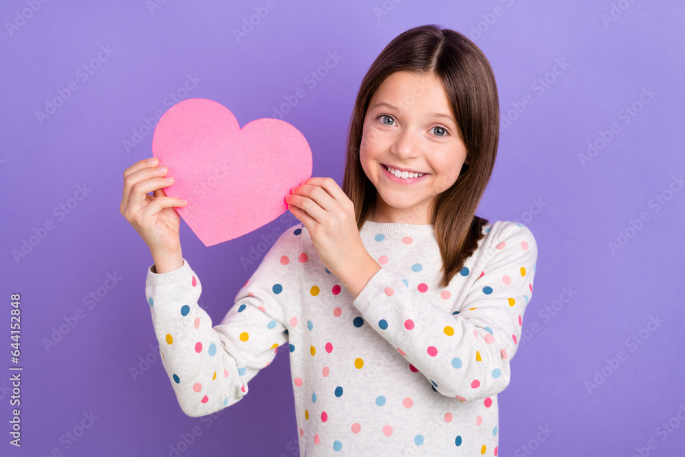 Photo of cheerful positive small girl wear dotted sweater rising pink heart isolated violet color background Photo of cheerful positive small girl wear dotted sweater rising pink heart isolated violet color background