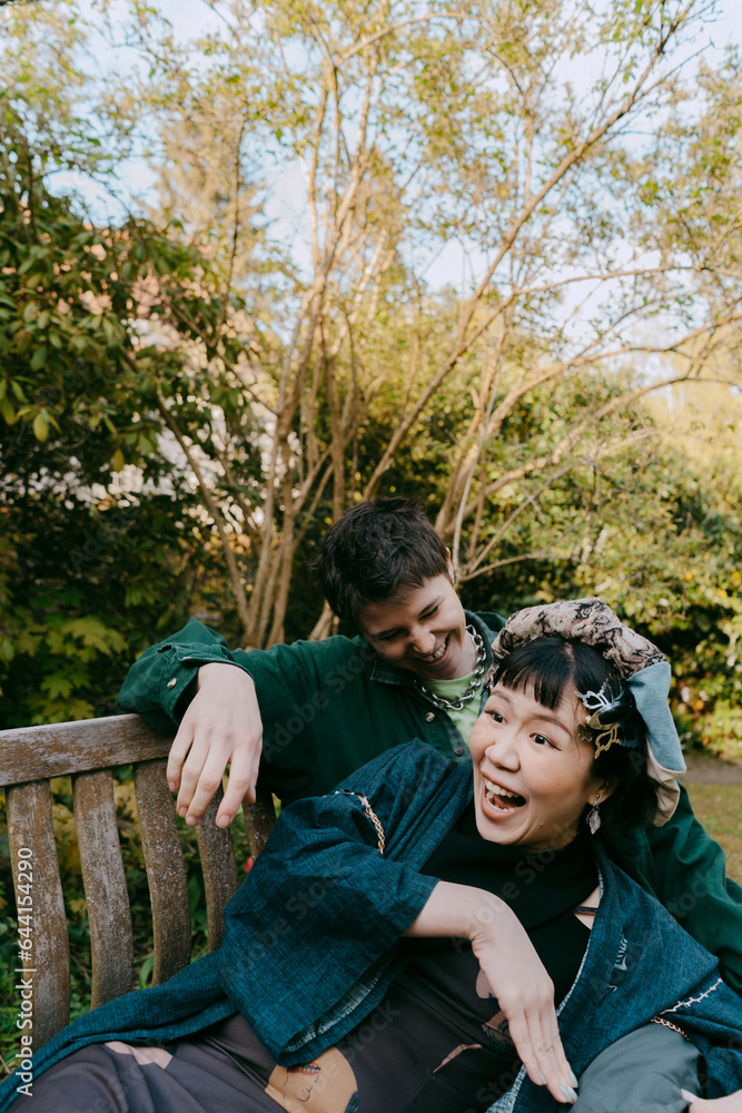 Cheerful LGBTQ friends enjoying together while sitting on bench during dinner party in back yard Cheerful LGBTQ friends enjoying together while sitting on bench during dinner party in back yard