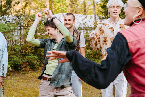 Happy non-binary person dancing amidts LGBTQ friends during party in back yard photo