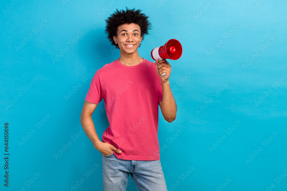 Portrait of cheerful guy with perming coiffure dressed stylish t-shirt hold loudspeaker arm in pocket isolated on blue color background