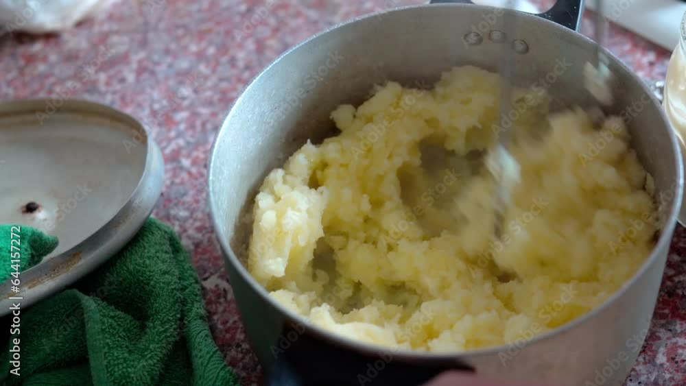 Man preparing tasty mashed potatoes in a steel saucepan in the kitchen, close-up top view. Freshly boiled puree with sour cream. Cooking process, of mash potato. Video footage in 4K 25FPS Man preparing tasty mashed potatoes in a steel saucepan in the kitchen, close-up top view. Freshly boiled puree with sour cream. Cooking process, of mash potato. Video footage in 4K 25FPS