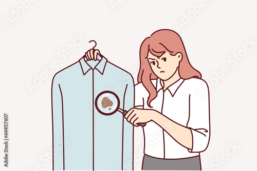 Woman detective holds shirt with blood stain and looks at screen in confusion, using magnifying glass to investigate crime. Smart girl detective found evidence on clothes of killer or monk