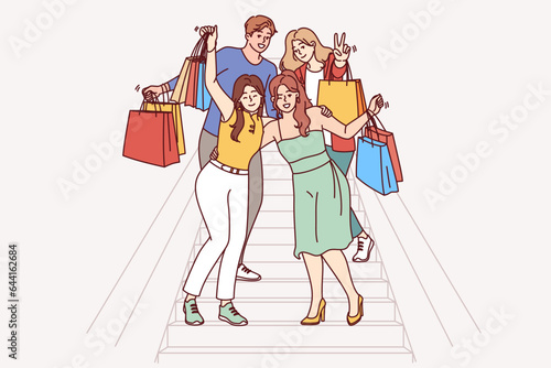 Group of shopaholics, mall buyers with multi-colored paper bags are standing on stairs, rejoicing at big discounts. Men and women shopaholics go to boutiques together and buy fashionable clothes
