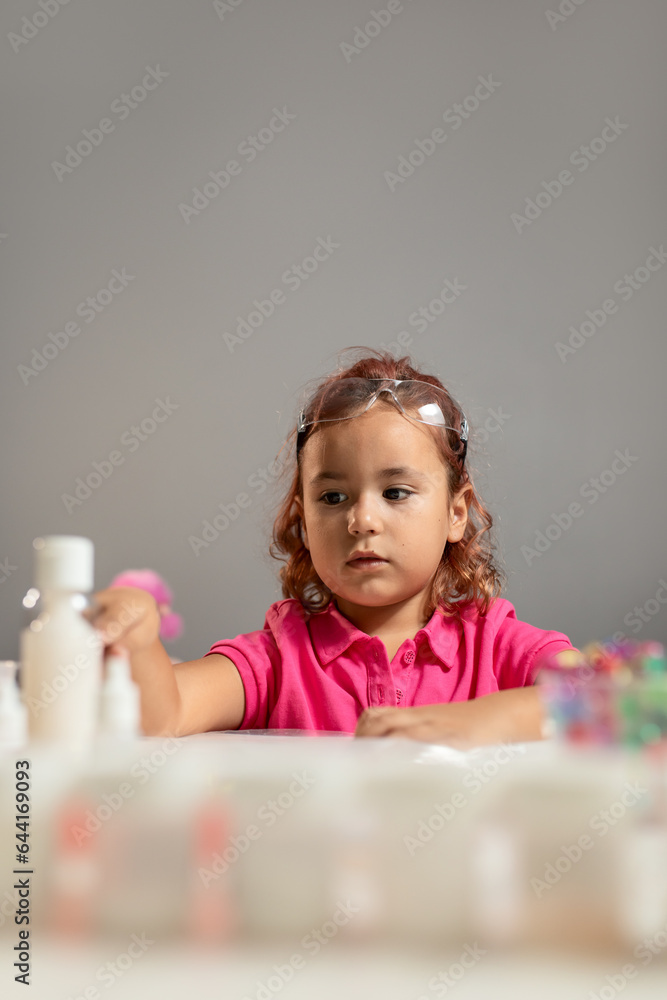 A beautiful little girl with crimson hair, wearing a pink shirt and safety glasses is playing educational games at the table A beautiful little girl with crimson hair, wearing a pink shirt and safety glasses is playing educational games at the table