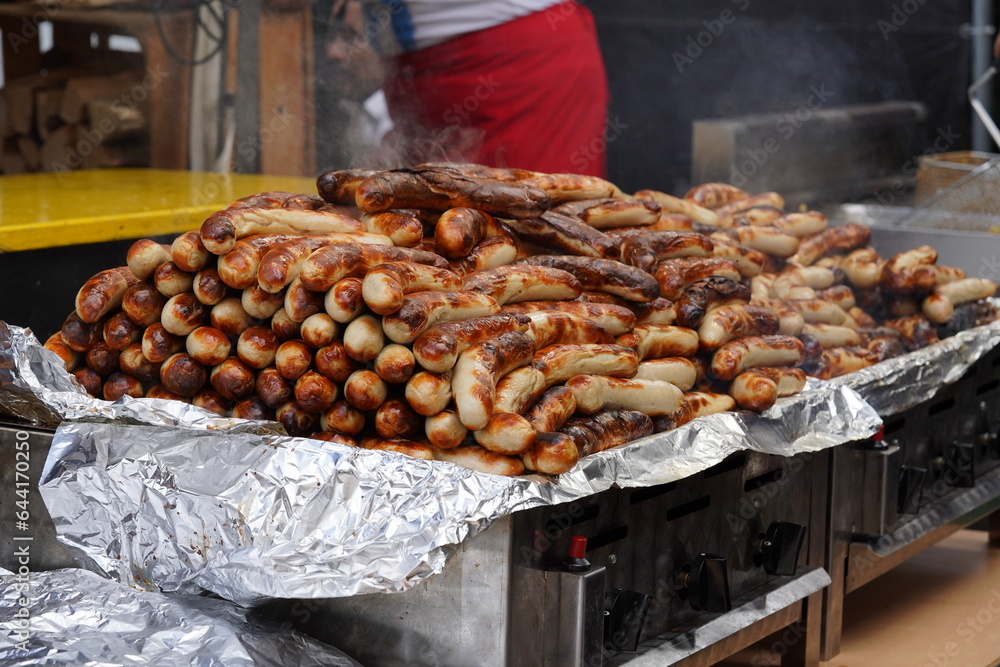 Roasted white sausages stacked and placed on an electric heater in order to keep them warm. They are exposed on a counter ready for sale. 