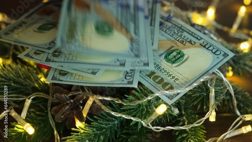 Hundred-dollar bills fall on a Christmas tree with a garland. Money and Christmas