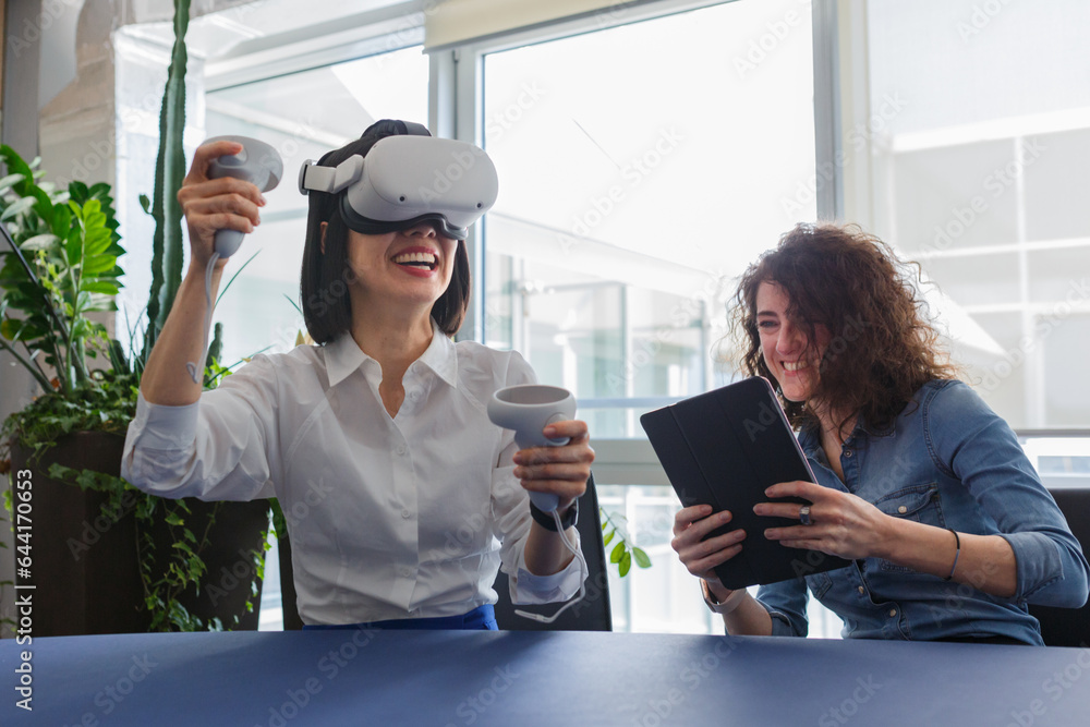 Tapet two women sitting at the table in the office and working with virtual reality vi