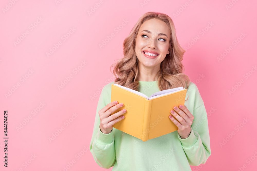 Photo of pretty creative minded lady toothy smile hold book look empty space isolated on pink color background Photo of pretty creative minded lady toothy smile hold book look empty space isolated on pink color background