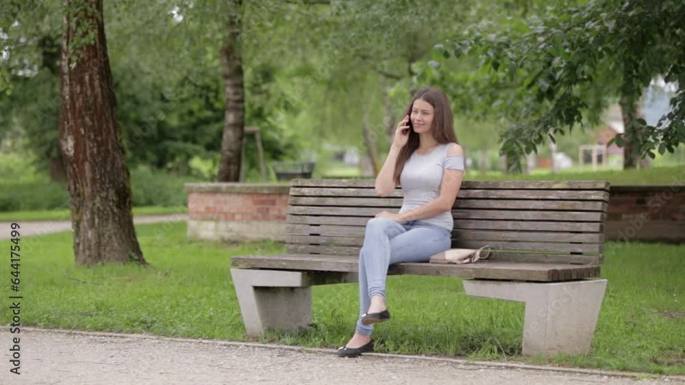 A girl sits on a bench in the park and talks on the phone. A girl sits on a bench in the park and talks on the phone.