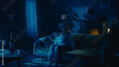 Fotografia Shot capturing a young woman sitting on the couch in a dark room