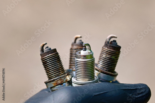 Spark plugs in hand of auto mechanic. Mechanic holding three old copper spark plugs and new one. Spark plugs replacement, repairing vehicle. Ignition troubleshooting of gasoline engine.