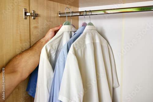 The man opens the closet and selects a shirt from the hanger.