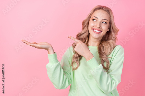 Photo of gorgeous positive lady toothy smile look direct finger arm hold empty space offer isolated on pink color background