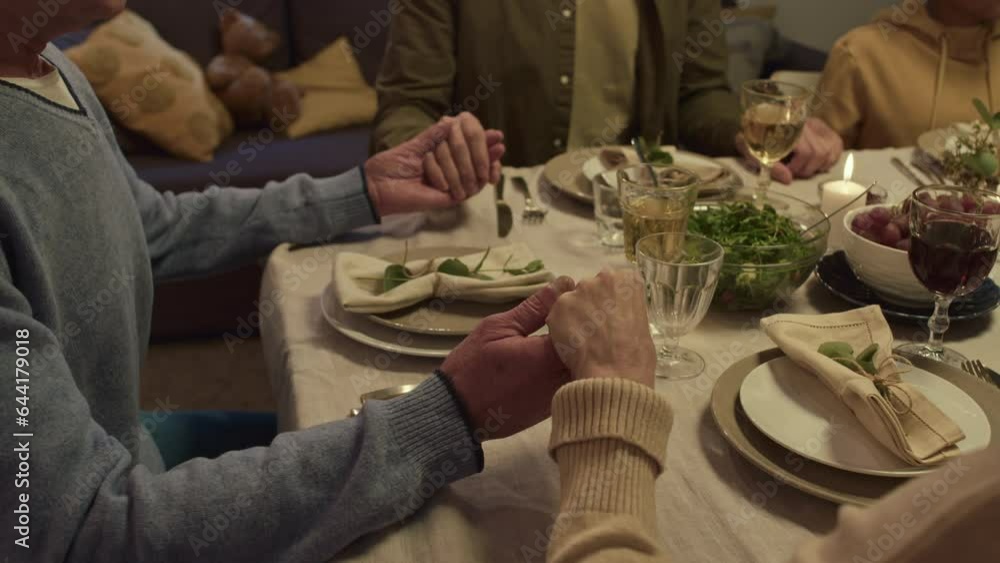 Cropped shot of family holding their hands while sitting at festive table and praying before dinner Cropped shot of family holding their hands while sitting at festive table and praying before dinner