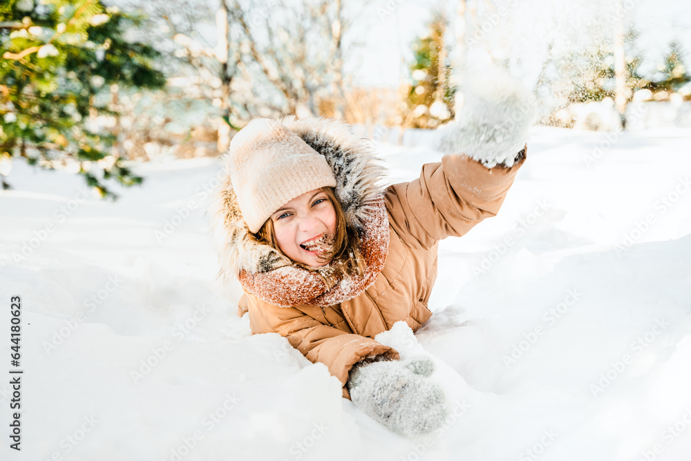 Φωτογραφία Little cute girl in beige hat,orange scarf snood is lying,playing in snow