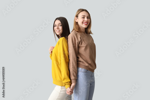 Female friends holding hands on light background