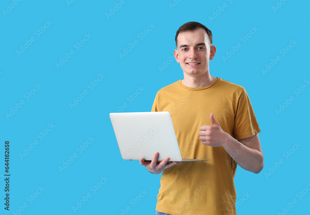 Young man with laptop showing thumb-up on blue background Young man with laptop showing thumb-up on blue background