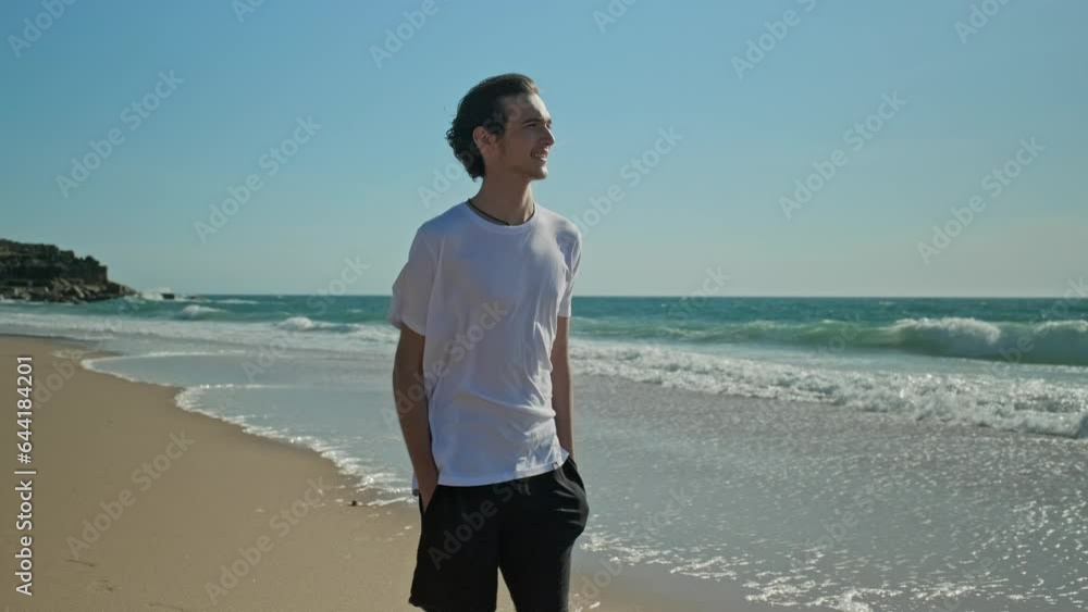 Happy young man walking on a sandy beach against background of the ocean on summer sunny day, slow motion. Young Male model walking along the sandy coast on summer. Smiling guy walks alone on a beach Happy young man walking on a sandy beach against background of the ocean on summer sunny day, slow motion. Young Male model walking along the sandy coast on summer. Smiling guy walks alone on a beach