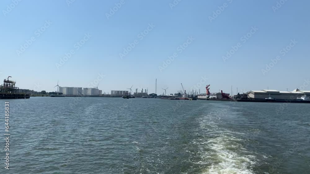 Wind turbines next to oil, petroleum storage at Port of Rotterdam. Spinning blades. Green, renewable energy, electricity generation. View from a moving boat. Rotterdam, North Holland, The Netherlands Wind turbines next to oil, petroleum storage at Port of Rotterdam. Spinning blades. Green, renewable energy, electricity generation. View from a moving boat. Rotterdam, North Holland, The Netherlands