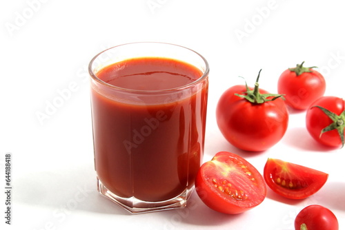 On a white background is a glass of tomato juice with tomatoes and herbs.